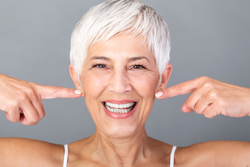Beautiful Caucasian smiling senior woman with short grey hair pointing at her teeth and looking at camera. Beauty photography.